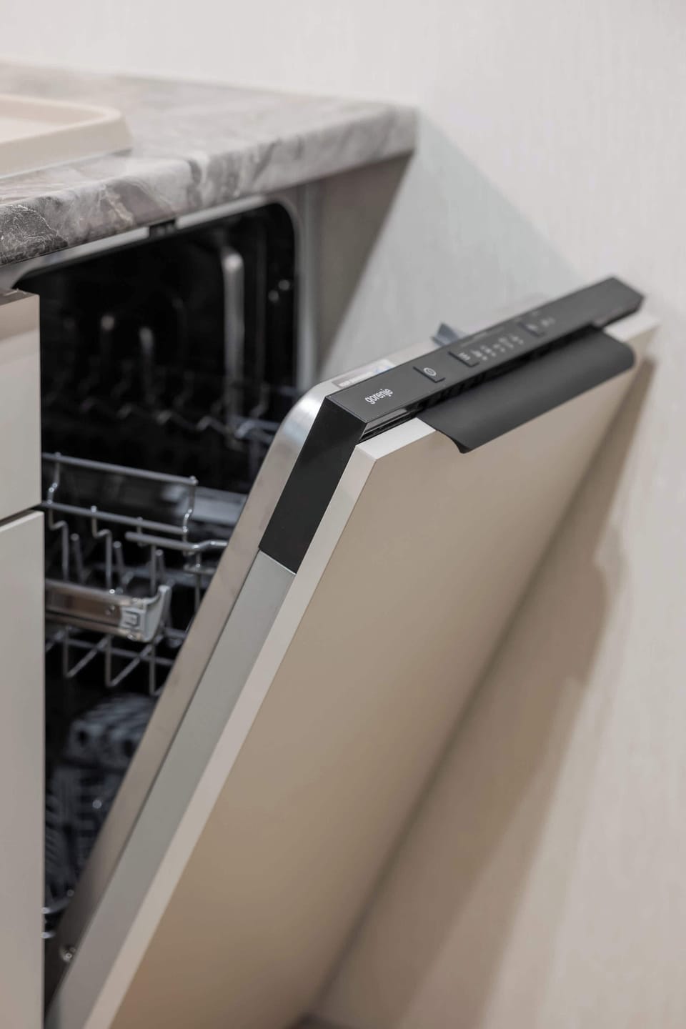 The interior of a modern dishwasher is shown partially open, revealing the sleek metal racks inside. It is built into the kitchen cabinetry beneath a dark countertop.