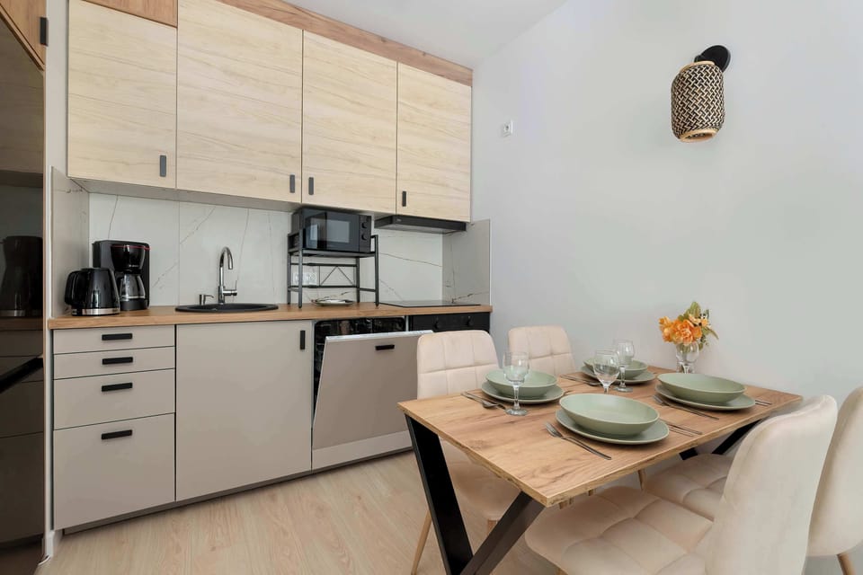 The kitchen area is shown from a wider angle, showing the cabinetry, appliances, and a table with chairs and place settings.