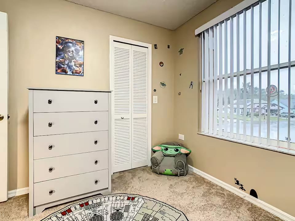 Bedroom corner with a white dresser, closet, and window with vertical blinds.