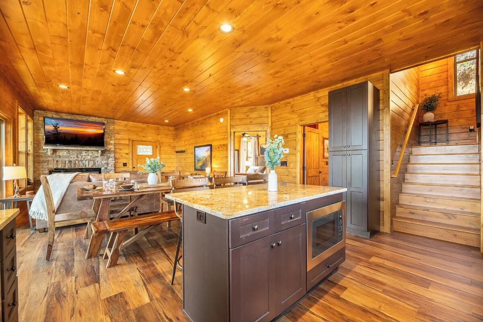 Warm wood surrounds you in this stunning open-concept cabin with granite island, stone fireplace, and rustic dining perfect for gatherings.