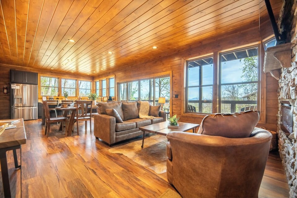 Warm wood surrounds you in this stunning open-concept living space, where leather furnishings invite relaxation and panoramic windows showcase relaxing wooded views.