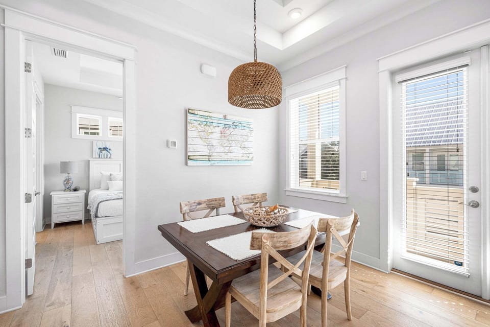 Bright dining area with coastal charm, rustic wood table, & woven pendant light.