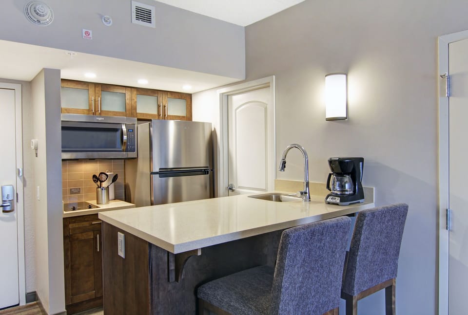Fully equipped kitchen with stainless steel fridge, overhead microwave, glass-front cabinets, and bar seating for two.