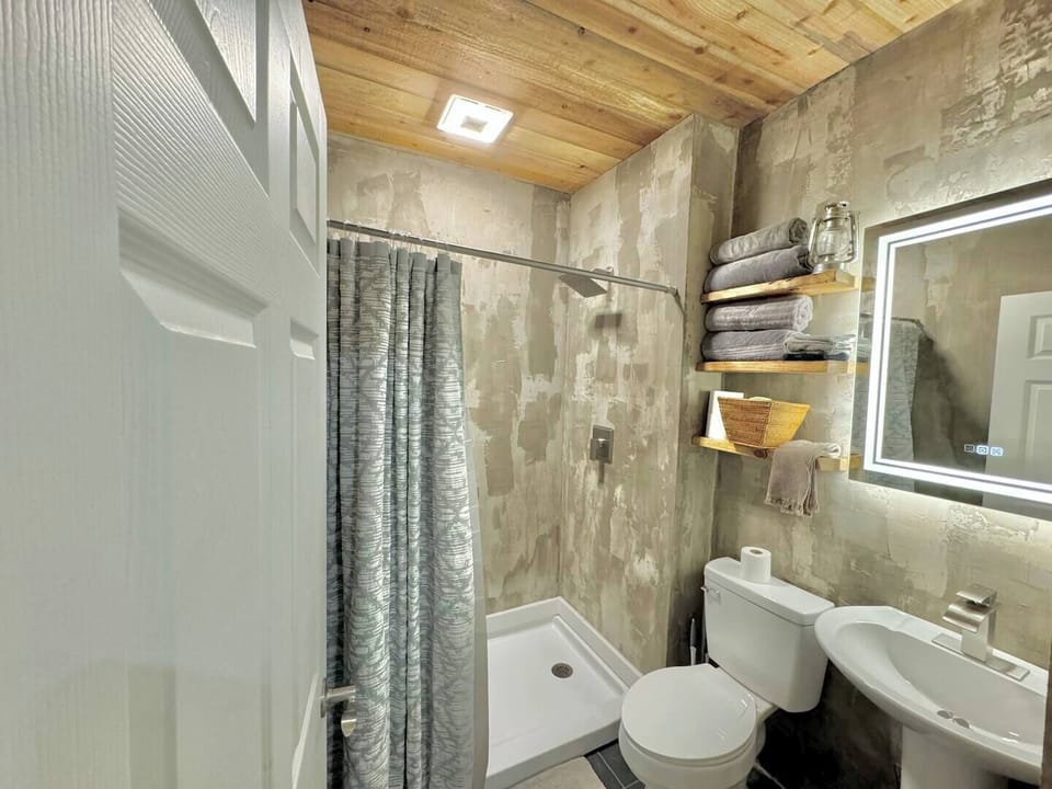 Experience urban chic in this sleek concrete bathroom, complete with a chic backlit mirror that adds a touch of ambiance to your morning routine. Step into a space where modern design meets relaxation, offering the ultimate cool vibes for your stay.