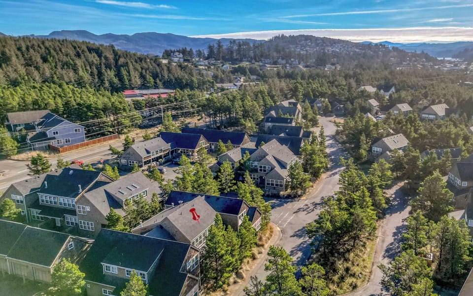 Aerial view of the vacation rental property nestled among forested hills and residential neighborhoods in a scenic mountain setting.