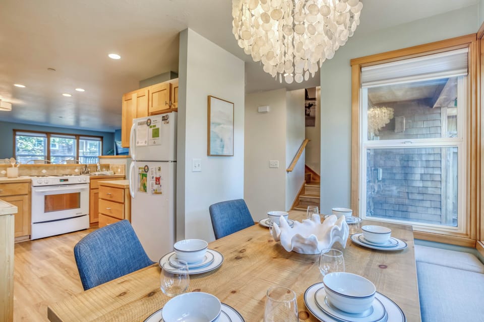 Your dining space glows with natural light from large windows, where a stunning shell chandelier illuminates intimate meals around the rustic wooden table.
