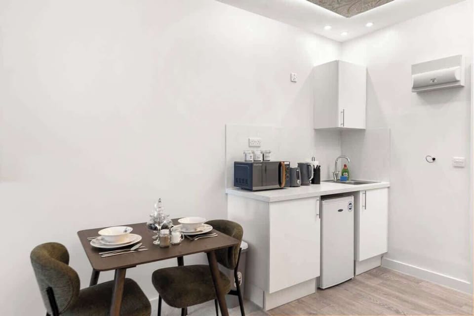 A cosy, modern dining area featuring a stylish table set for two, perfect for relaxed meals. Positioned beside the sleek kitchenette, it offers a bright, inviting space ideal for breakfasts, dinners, or planning your day ahead.