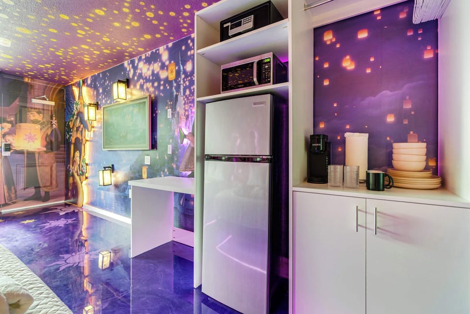 Compact kitchenette area with a refrigerator, microwave, and coffee maker against a purple lantern-themed wall.