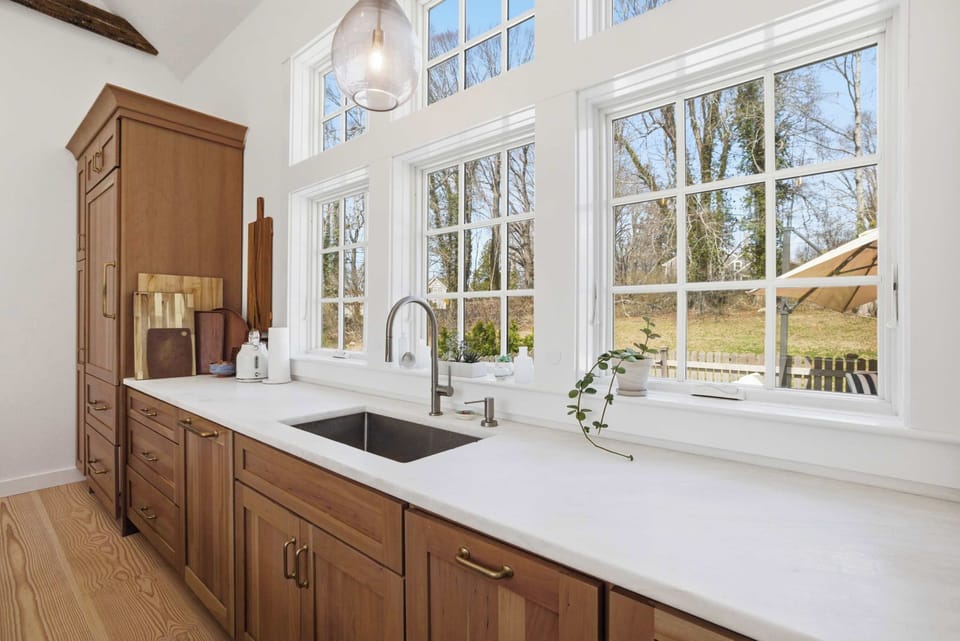 The sink side of the kitchen catches the backyard light through large windows — walnut cabinetry, quartz counters, and room to work.