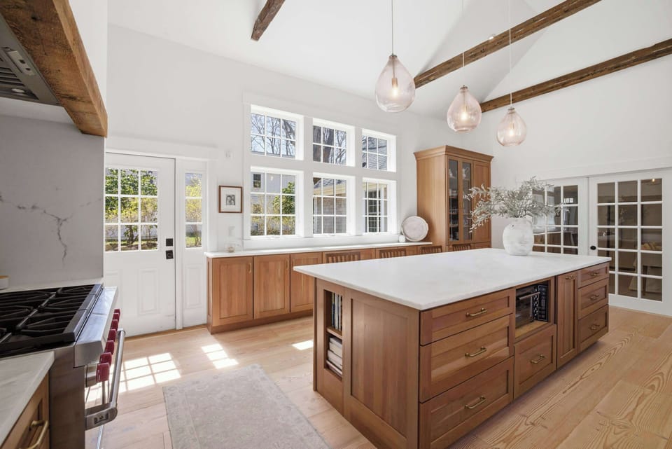 Original hand-hewn beams cross above the Wolf range alcove, where the raw wood hood surround bridges the home's history with a fully professional kitchen.