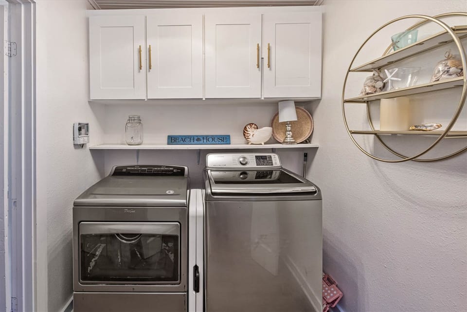 Laundry room with washer and dryer, overhead storage cabinets, and functional shelving.