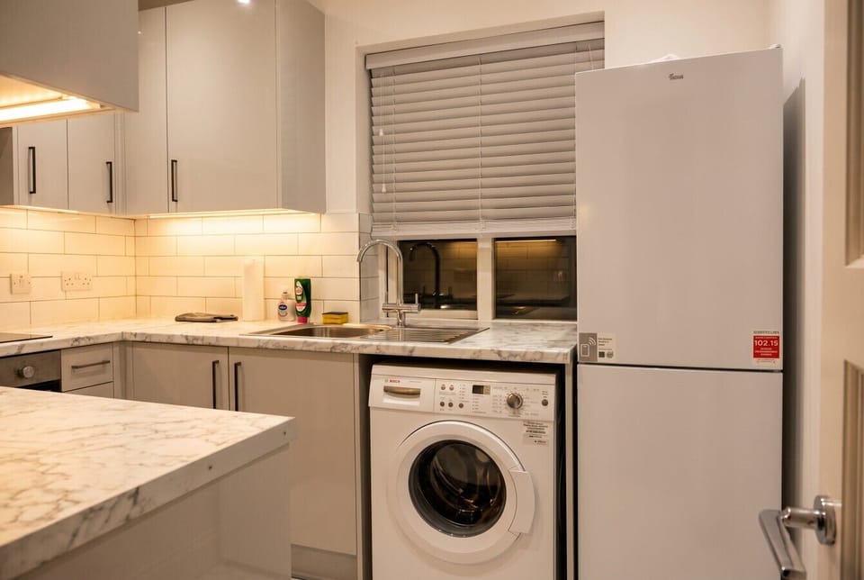 Kitchen sink area with marble counters, integrated washing machine and tall fridge for practical everyday living.