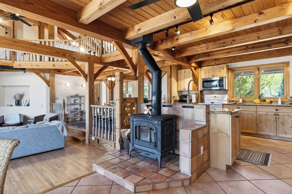 A warm, open-concept living space anchored by a wood-burning stove and rich timber beams—perfect for cozy nights in.
