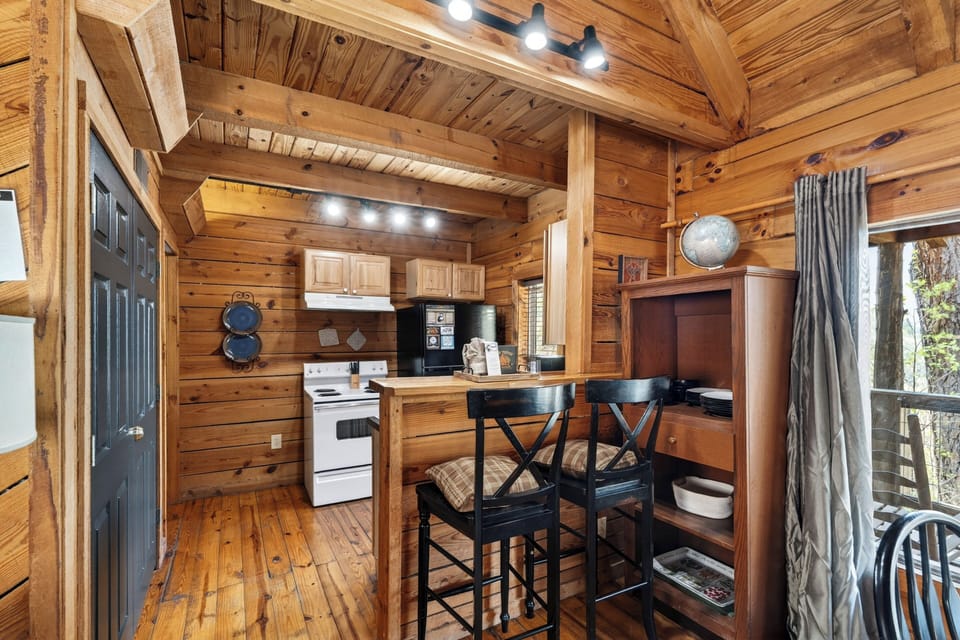 Rustic cabin kitchen with warm wood walls, a cozy breakfast bar, and soft natural light from the window.