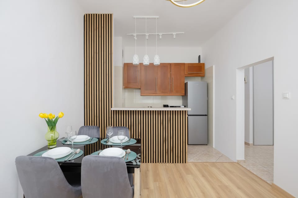 An open-plan interior connecting the living area with a kitchenette, highlighted by wooden cabinetry and clean lines. The space feels practical and well-organized, with subtle decorative touches.