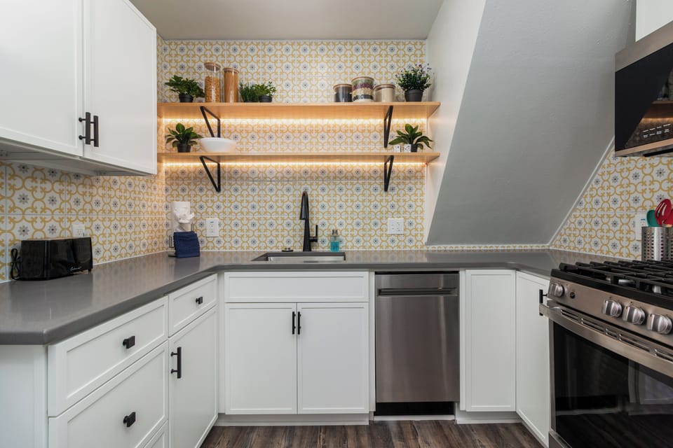 Your bright, modern kitchen features beautiful patterned backsplash tiles, sleek white cabinets, and open shelving adorned with fresh plants.