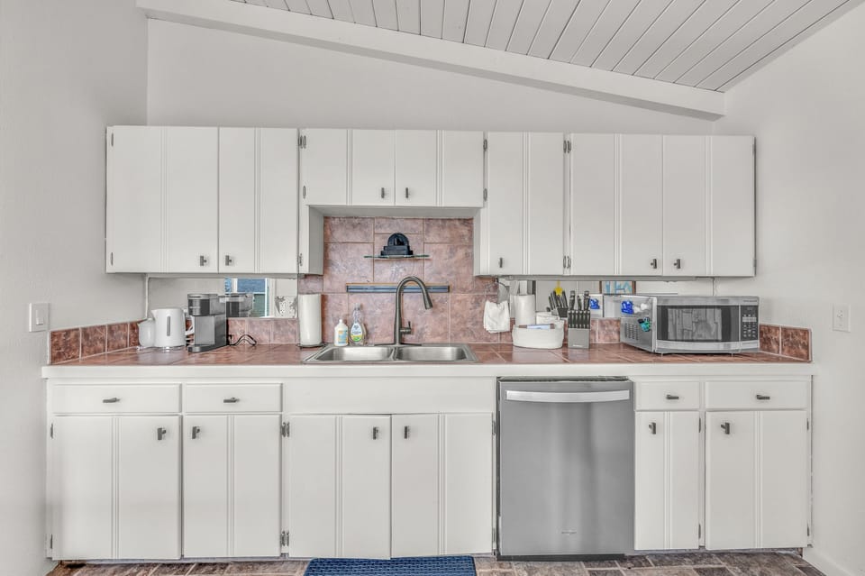 Your fully equipped kitchen features white cabinets, stainless steel appliances, and a charming brick backsplash perfect for preparing meals during your stay.
