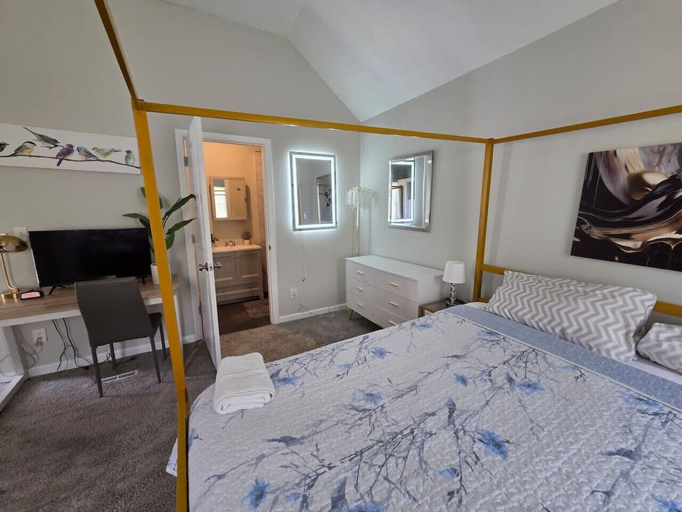 Relax in this elegant and spacious primary bedroom, anchored by a stunning gold-frame canopy bed dressed in high-quality floral and geometric linens. The room doubles as a functional retreat, featuring a dedicated workspace with a desk, chair, and flat-sc