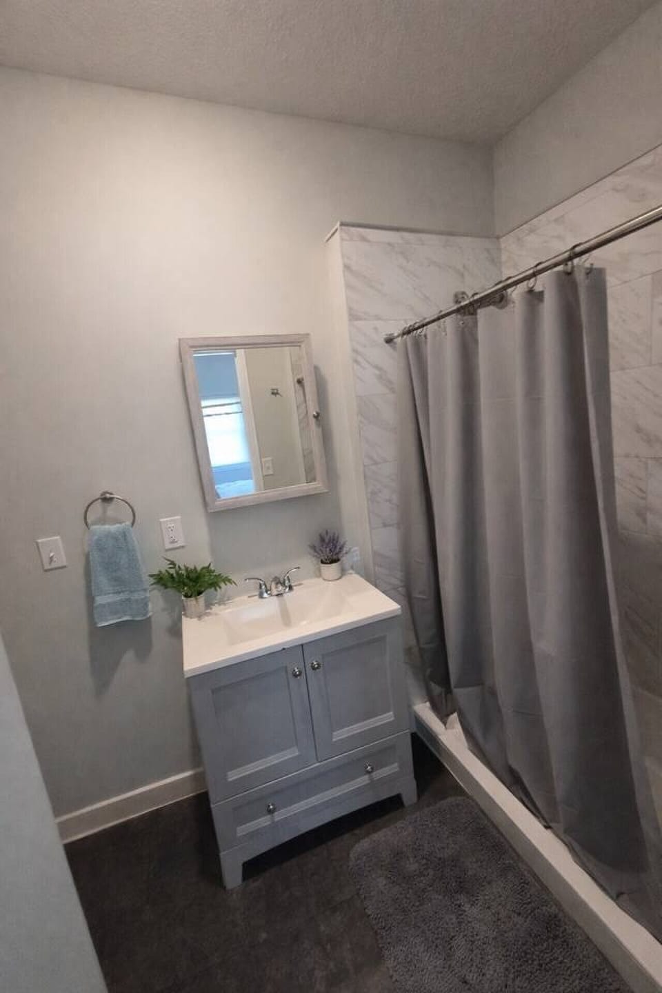This clean and contemporary bathroom features a stylish grey vanity topped with a crisp white sink and modern chrome fixtures. A framed medicine cabinet mirror offers convenient storage and functionality, while the walk-in shower is beautifully finished w