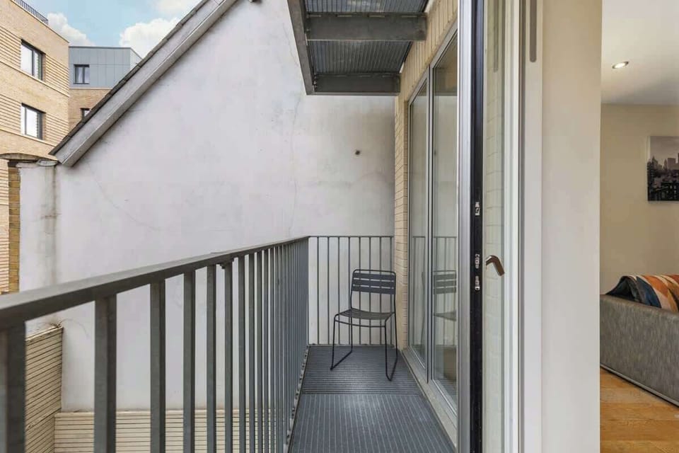 Step out onto the metal-decked private balcony equipped with slim steel railings, a minimalist chair, and sliding glass entry doors leading into the main living room.