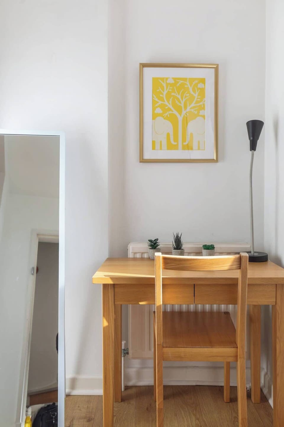 Focus or study comfortably at this dedicated wooden desk nook, featuring a matching wooden chair, a modern slim black floor lamp, full-length mirror, and vibrant yellow framed wall art.