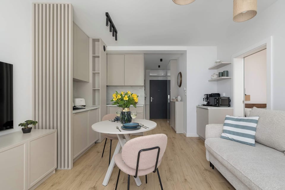 An open-plan living room and kitchen with a TV, cabinets, and a dining area. The design emphasizes functionality and simplicity.