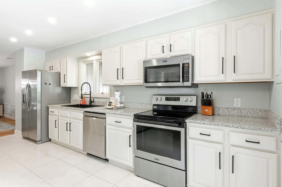 Creamy white cabinetry and speckled stone surfaces create a tidy, luminous workspace for your morning coffee. Modern stainless appliances shimmer under soft recessed lighting, offering a sleek yet homey atmosphere for every meal.