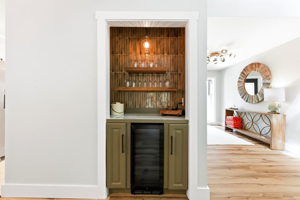 Bronze tiles and floating timber shelves create a moody, sophisticated bar nook perfect for evening pours. Soft amber glows from the pendant light, highlighting the crisp glassware and olive cabinetry in this stylish entertaining corner.