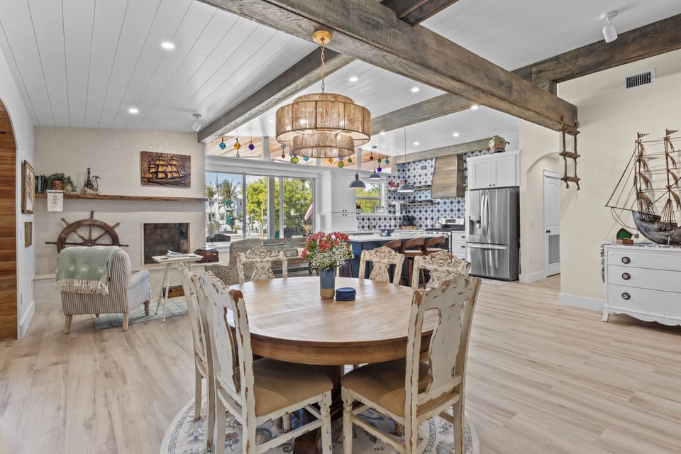 Gather around your coastal-inspired dining table beneath soaring beamed ceilings, where nautical charm meets modern comfort in this open living space.