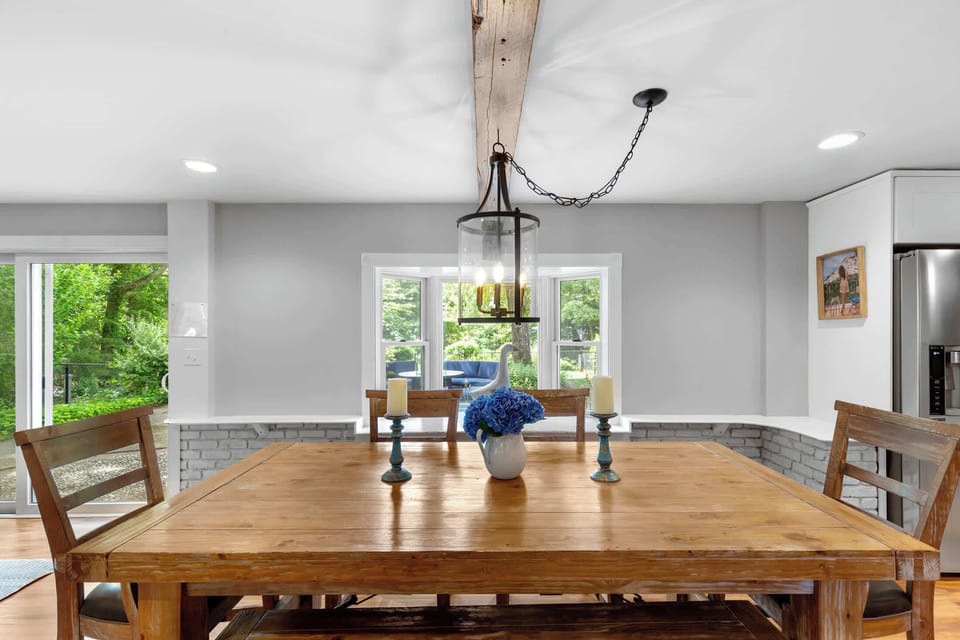 The dining area sits beside the statement fireplace, blending rustic beams and natural light for shared dinners after the beach.