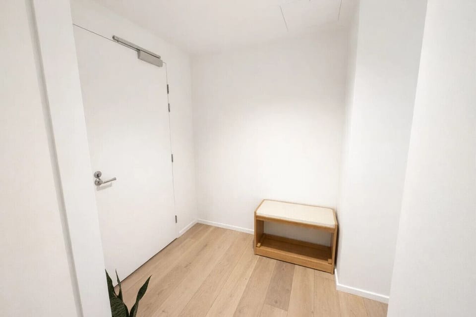 Clean, minimal entryway with warm timber flooring, a compact shoe bench, and a solid entry door — a calm, uncluttered welcome into the apartment.