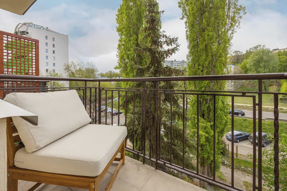 Another balcony angle showing cushioned seating and metal railings overlooking a green residential area. The space is ideal for relaxing outdoors.