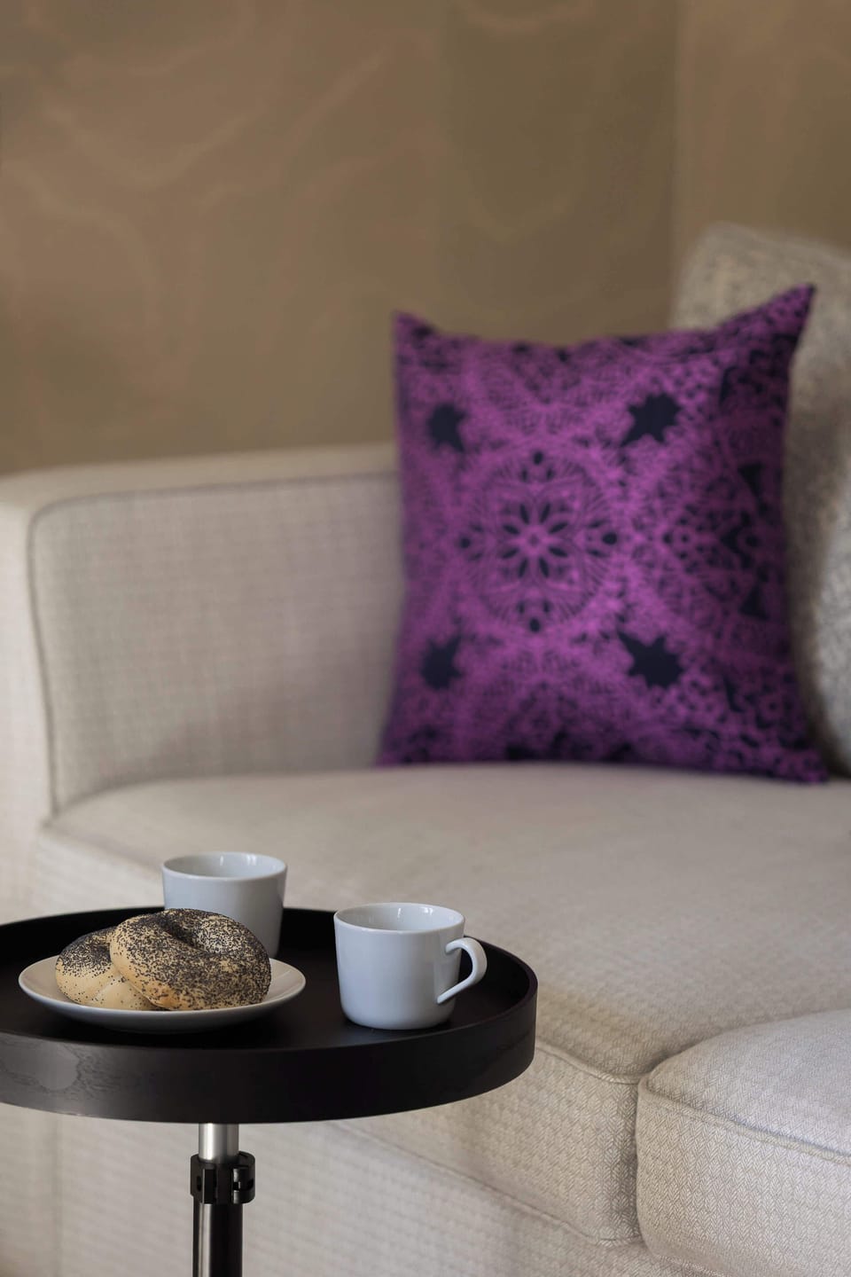 A comfortable sofa corner styled with a purple accent pillow and a small round coffee table. The arrangement feels intimate and perfect for relaxing.