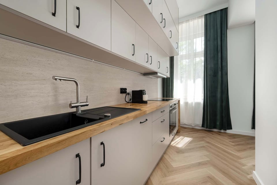 A sleek kitchenette with light cabinetry, a wooden countertop, and a black sink. Upper cabinets provide ample storage, while the long counter offers practical workspace.