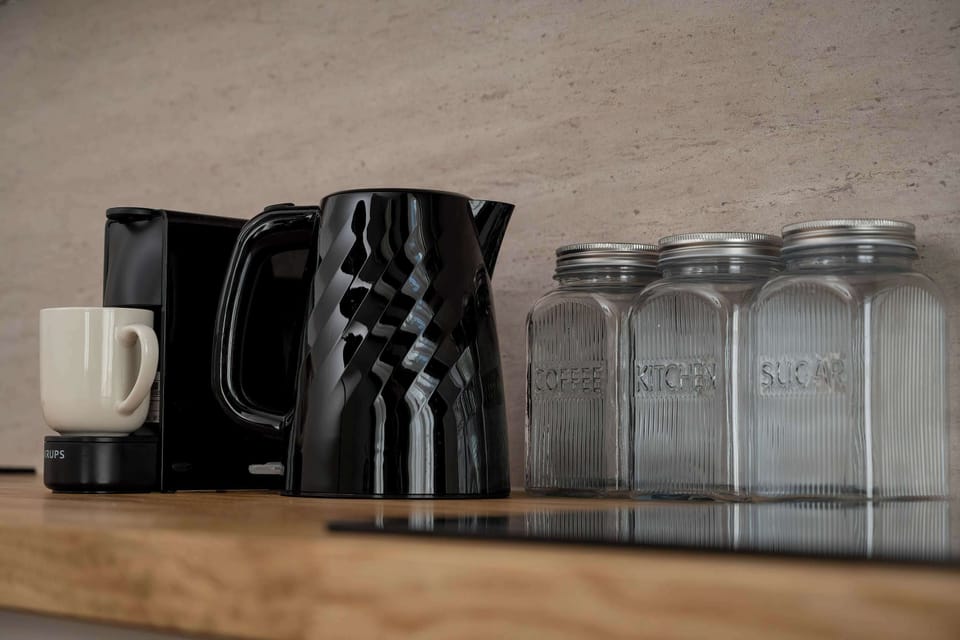 A close-up of a kitchenette countertop with a kettle, coffee machine, and neatly arranged glassware. The wooden surface adds warmth, while the appliances provide everyday convenience.