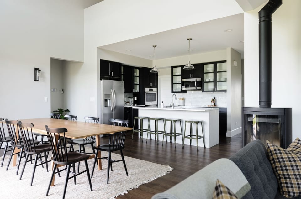 The open-concept great room flows seamlessly from the dining table to the kitchen, anchored by a sleek wood-burning stove.