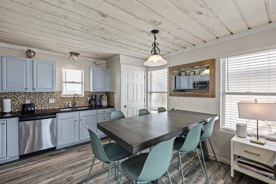 Open dining area with large table, pendant lighting, and bright kitchen space ideal for family meals during beachfront vacations.