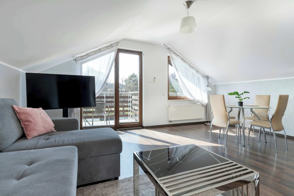 A stylish open-plan living room with a sofa and a TV near large windows. The room is bright and airy with a modern touch.