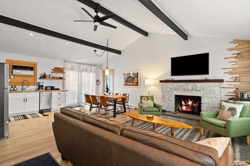 Living room with mounted TV, stone fireplace, and exposed beams