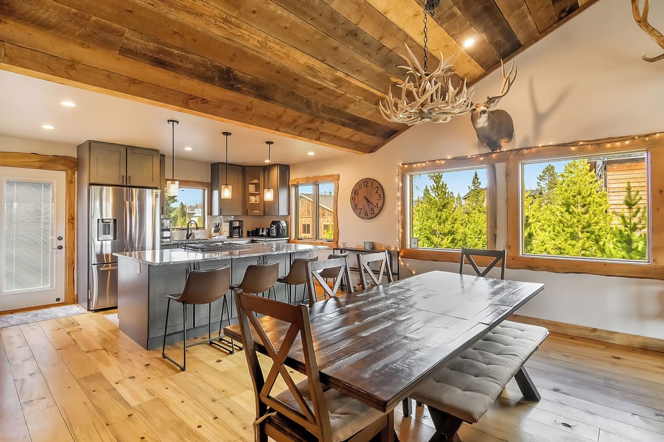 Gather around this stunning rustic dining space with exposed beams, modern kitchen, and forest views for memorable mountain meals together.