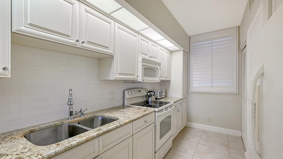 Galley kitchen with granite countertops, white cabinetry, tiled backsplash, and stainless steel double sink.