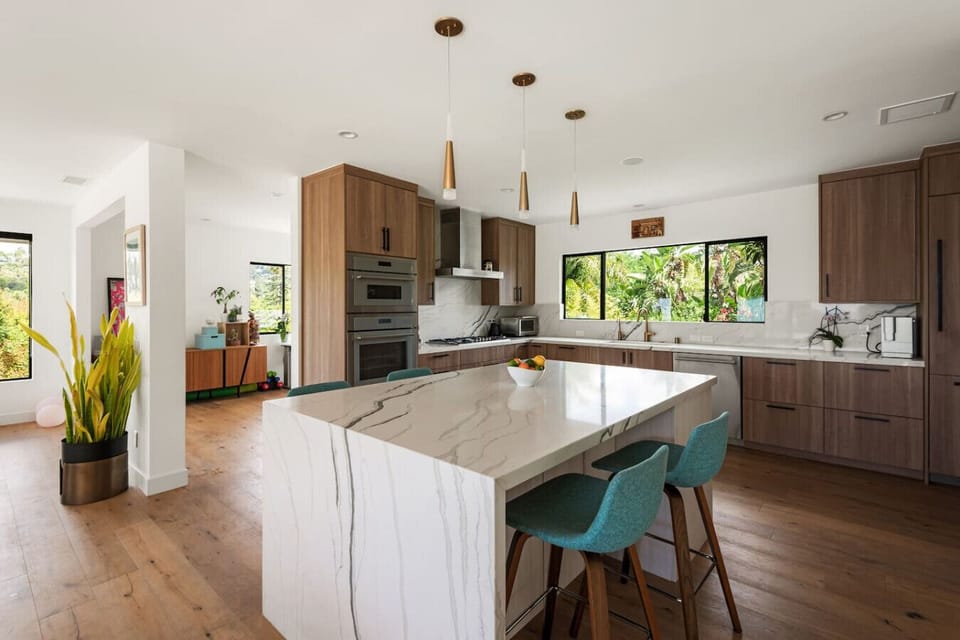 A stunning chef`s kitchen featuring a dramatic marble waterfall island, warm walnut cabinetry, pendant lighting, and garden views — as beautiful as it is functional.