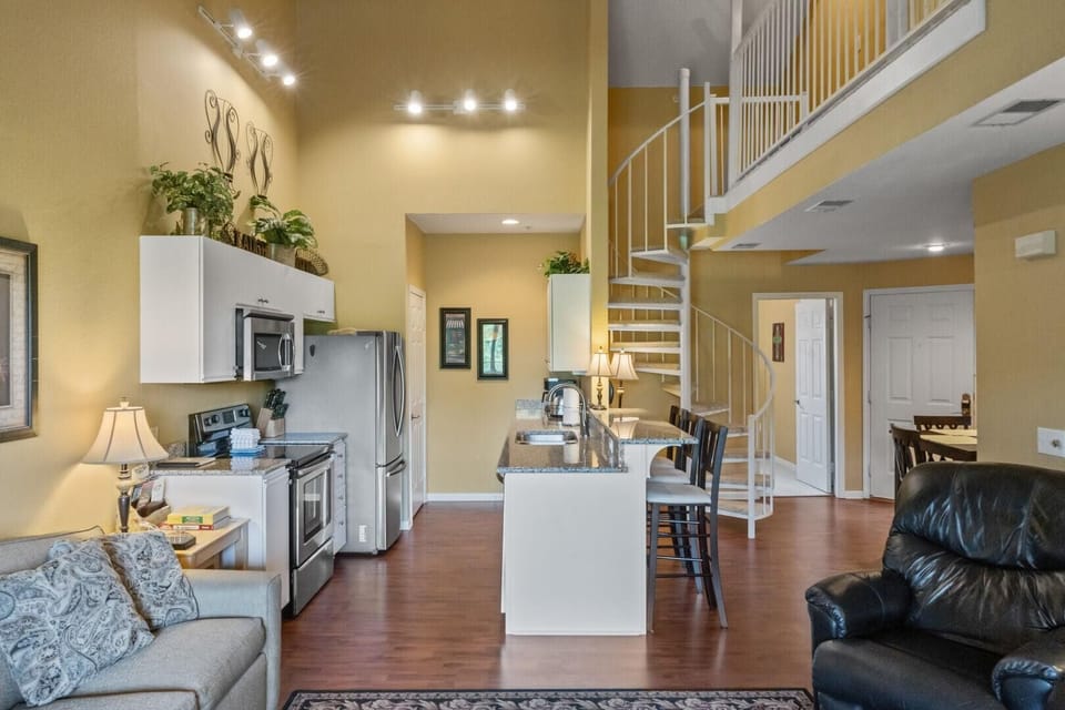 Kitchen features granite countertops, stainless steel appliances, and a white spiral staircase leading upstairs.