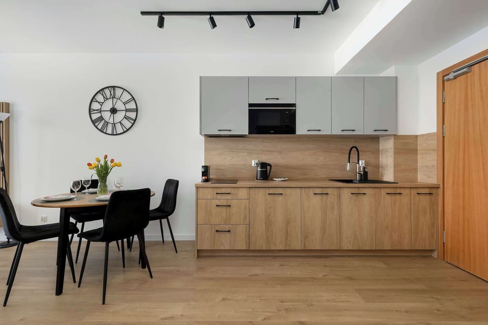 A compact kitchenette space with light wood cabinets and a small dining table placed nearby. The area feels functional and cozy, with simple decor and neutral tones dominating the interior.
