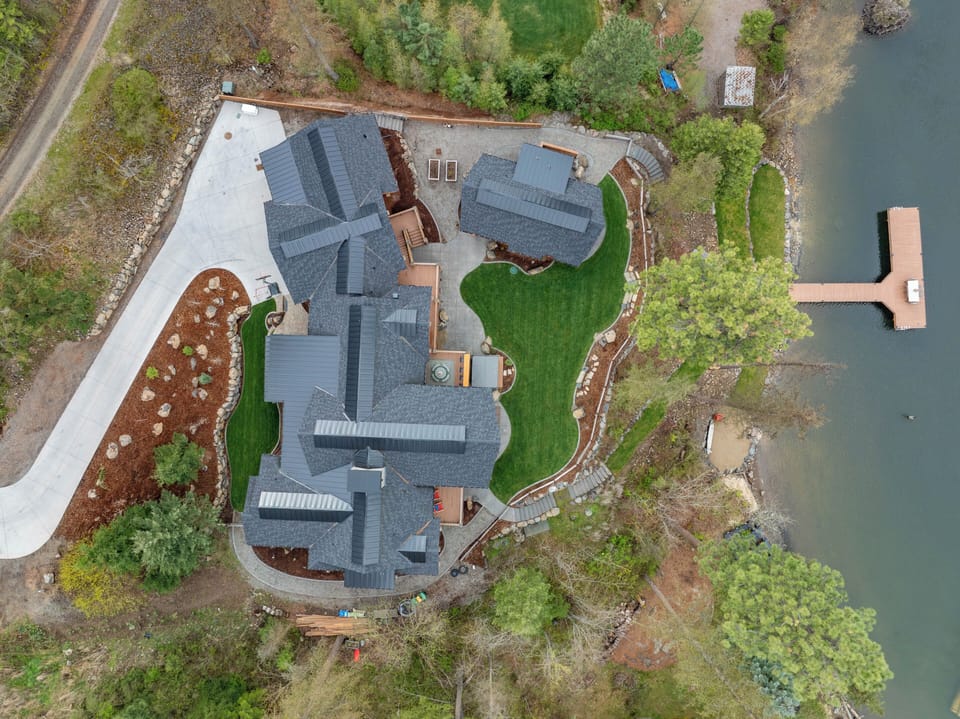 Bird's-eye aerial revealing the full footprint of the property, private grounds, and the sparkling water just steps away.