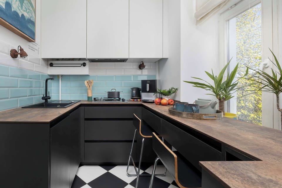 A modern U-shaped kitchen with black cabinet fronts and a wooden countertop that also serves as a bar with high stools. 