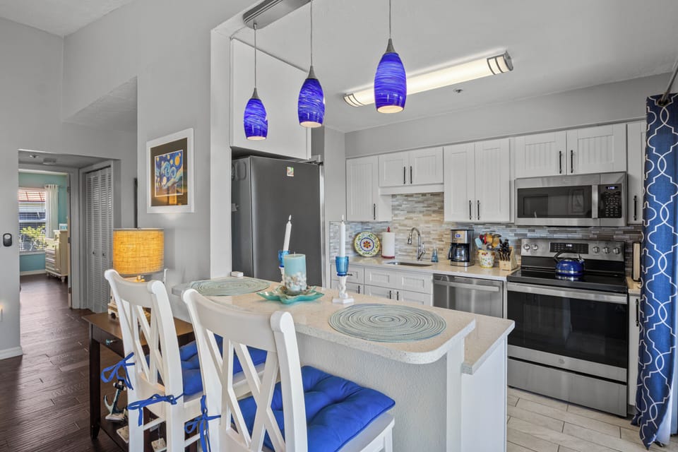 Your stylish kitchen features stainless steel appliances, coastal blue accents, and a breakfast bar perfect for morning coffee or evening cocktails.