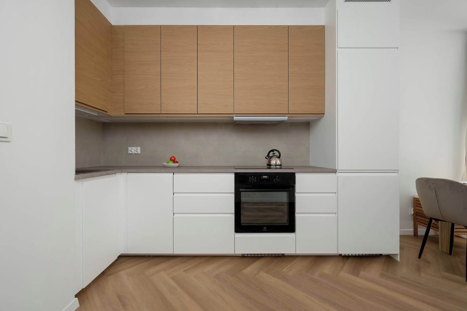 A wider view of the open-plan kitchenette and living area, showing a seamless connection between cooking and dining spaces. The combination of modern finishes and warm flooring creates a balanced and comfortable interior.