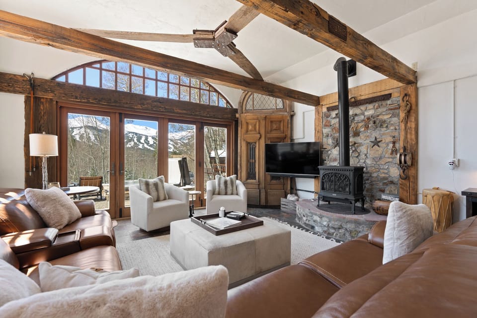 Unwind in this stunning living room where rustic beams meet modern comfort. Sink into plush seating by the stone fireplace, enjoy mountain views through expansive windows, and relax in your elegant alpine retreat.