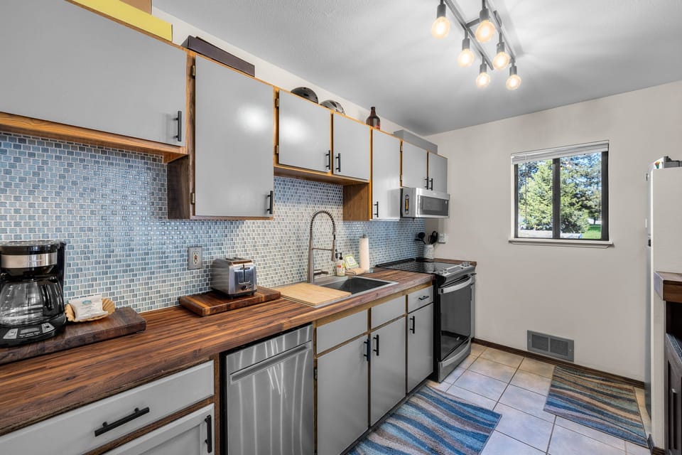 Your fully equipped kitchen features modern appliances, butcher-block counters, and a stunning blue mosaic backsplash perfect for preparing memorable meals.